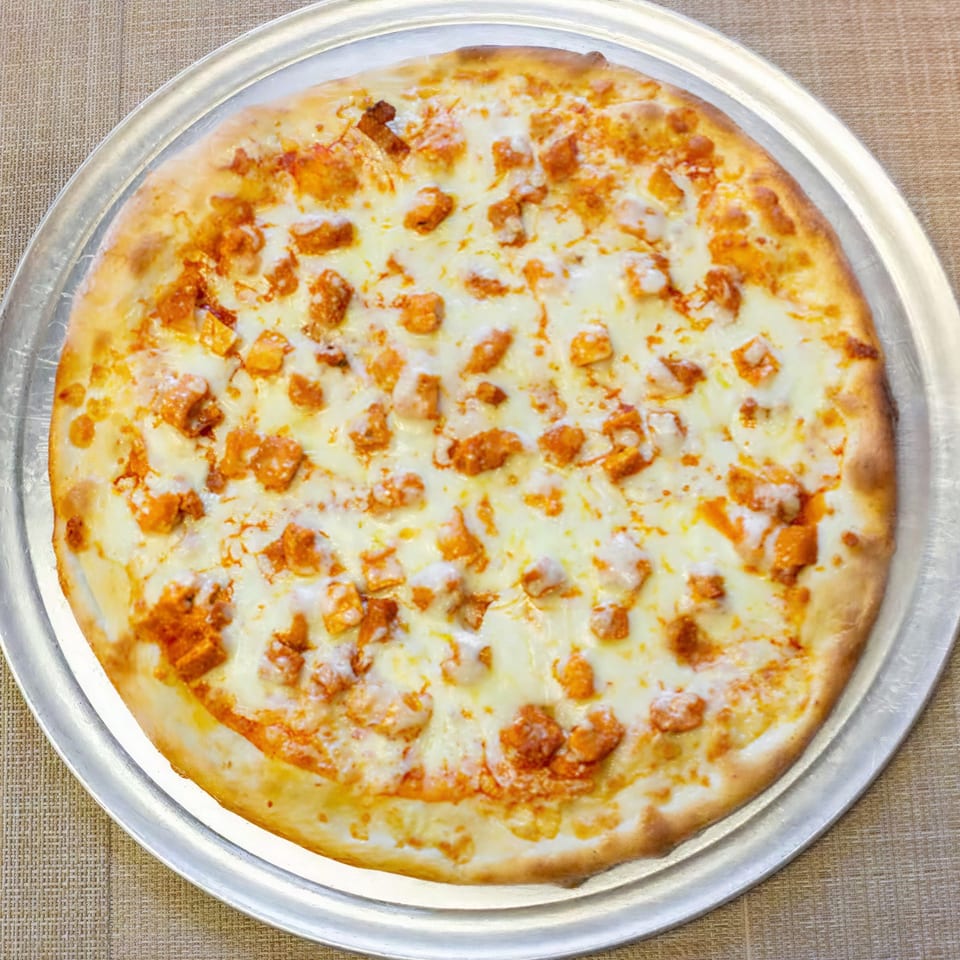 A whole buffalo chicken pizza with white cheese and orange chicken pieces on a metal tray.