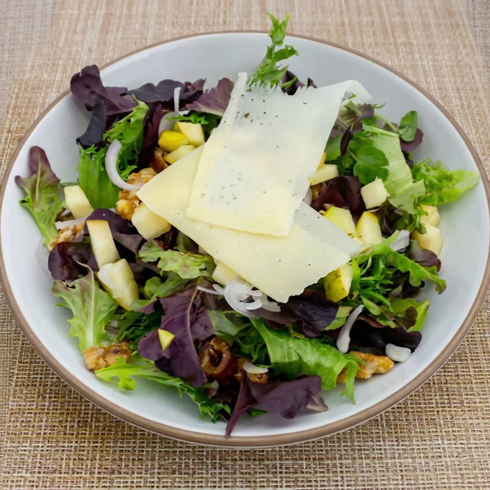 A fresh salad with mixed greens, sliced pears, walnuts, red onion, and shaved cheese in a white bowl.