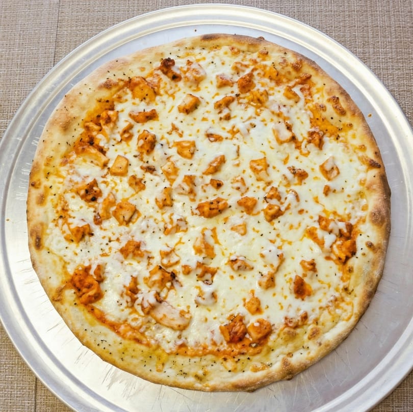 A whole buffalo chicken pizza with white sauce and mozzarella cheese on a metal tray.