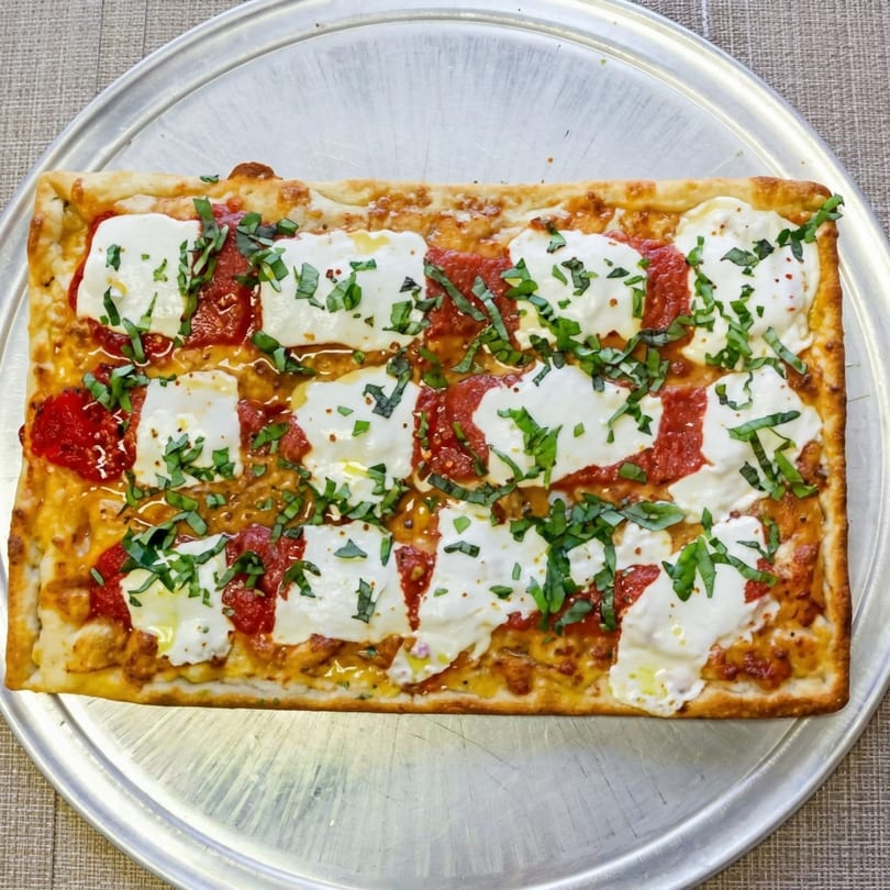 Rectangular pizza with red sauce, fresh mozzarella, and basil on a metal tray.