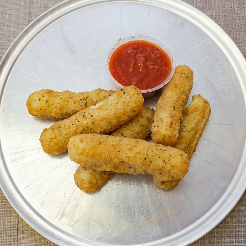 Golden-brown mozzarella sticks with herbs and a side of red marinara sauce on a metal tray.