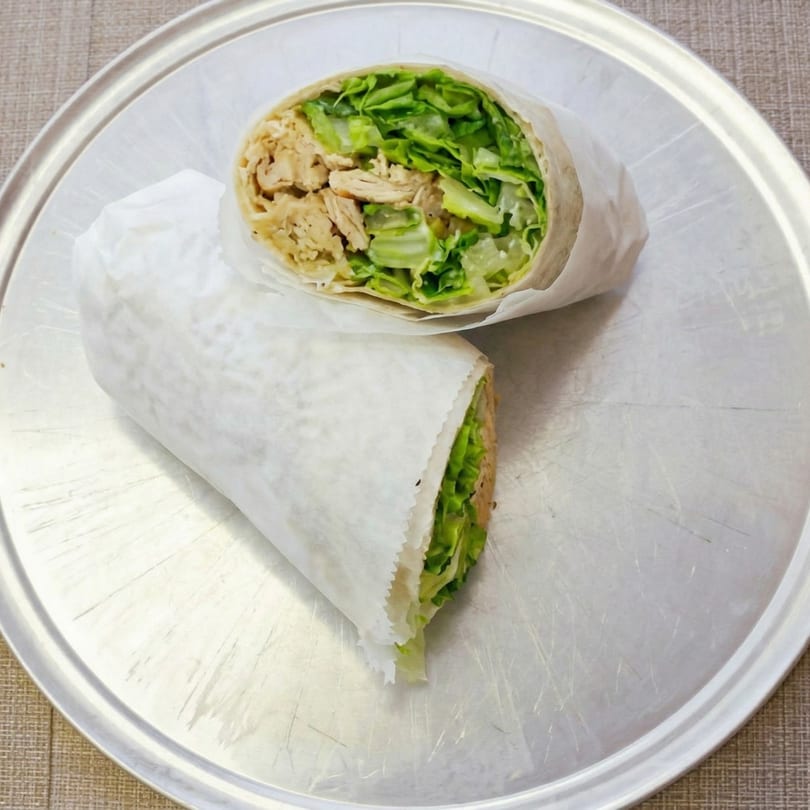 Two chicken and lettuce wraps, partially unwrapped, on a round metal tray.